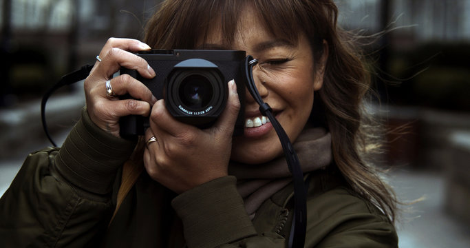 Street photographer smiles while taking a photo of her subject with a professional digital camera