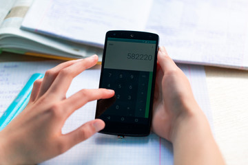 Beautiful young teenage school girl studying with smartphone, close up on hands with the mobile phone.