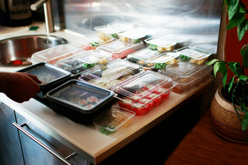 A large number of boxes of sushi are laid out on a large festive table. The hosts of the holiday are awaiting guests.On the table Sushi of dift colors and sizes.  Nearby is a plant.