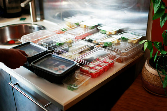 A large number of boxes of sushi are laid out on a large festive table. The hosts of the holiday are awaiting guests.On the table Sushi of dift colors and sizes.  Nearby is a plant.