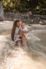 Fototapeta premium Happy smile european family have rest and run on white sand beach. Father, long black chestnut hair mother, blond baby boy. white cotton clothes. boho dress. t-shorts.Thailand. Aquamarine crystal sea