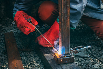 A welder welds a metal pole with electric welding, holds an electrode in his hands
