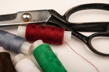 Several reels of multicolored sewing thread and large vintage sartorial scissors on a white background. Close up.