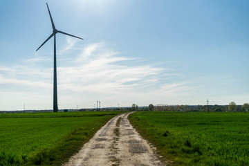 Wind turbine standing near the dirt road and green fields in Poland