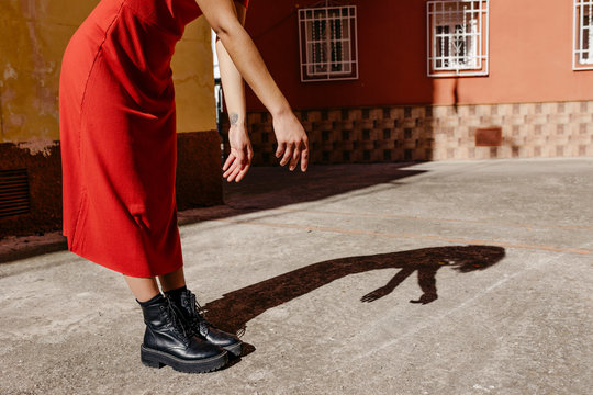 Young woman wearing red dress and black boots, playing with her shadow on the floor