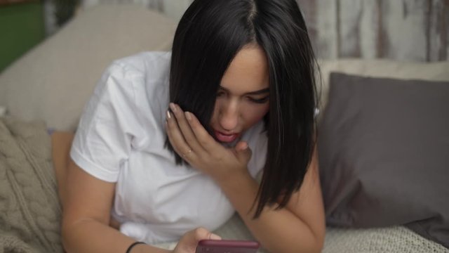Young Asian Female is Reading News or Messages in a Smartphone at Home in a Comfortable Apartment and Gets Shocked Dissatisfied Worried and Sad, Close Up