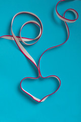 Heart shaped with decorative ribbon on rough blue paper. Textile white ribbon with pink line. Heart care concept.