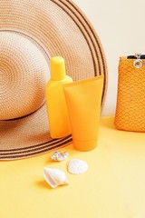 Summer cosmetic products for skin hydration. Sun hat, yellow sunscreen bottle, sunblock tube, cosmetic bag and seashells