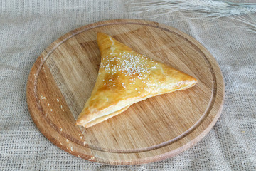  Uzbek triangular samsa of puff pastry on a round kitchen board on a background of burlap