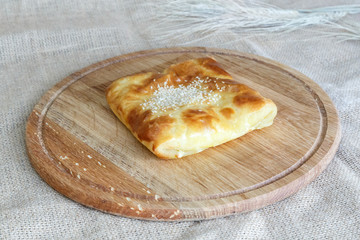 Appetizing Uzbek square samsa made of puff pastry on a round kitchen board on a burlap background