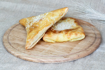 Asian square and triangular samsa with puff pastry sesame seeds on a wooden kitchen board on burlap background