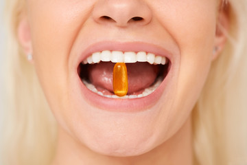 Beautiful woman mouth with pill In teeth. Girl taking vitamins