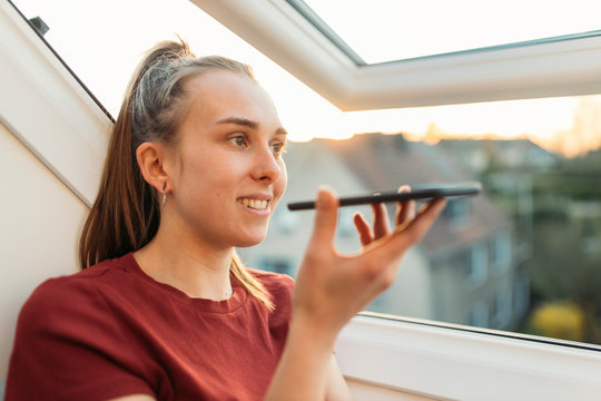 Young woman using smartphone at the window in backlight