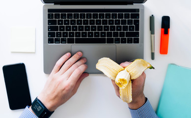 Spain, Hands of man typing on laptop and eating banana