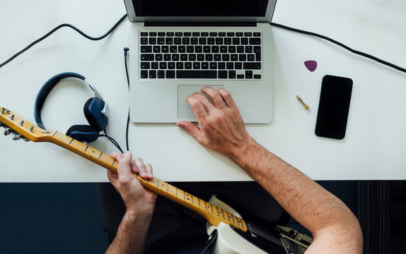 Topf view of man learning to play electric guitar online using laptop