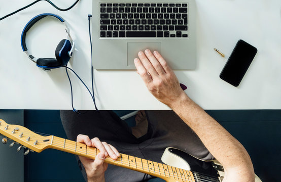 Topf view of man learning to play guitar online using laptop