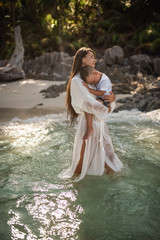 Happy smile european family have rest and run on white sand beach. Father, long black chestnut hair mother, blond baby boy. white cotton clothes. boho dress. t-shorts.Thailand. Aquamarine crystal sea