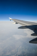 Obraz premium View over the clouds from the porthole of an airplane with plane wing and blue sky
