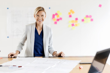 Portrait of happy blond businesswoman in conference room with adhesive notes at whiteboard