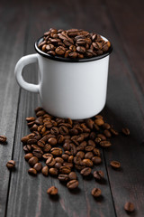Closeup view of white metal mug overfilled with spilling coffee beans