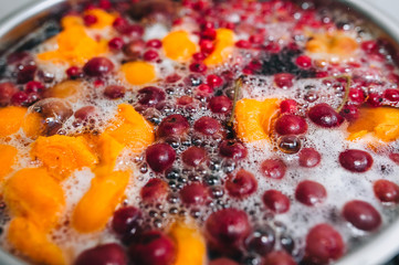 Fresh fruits: apricots, cherries, raspberries, apples are boiled in boiling water in a metal pan on a stove with bubbles and foam close-up. Cooking delicious homemade compote. Photography, concept.