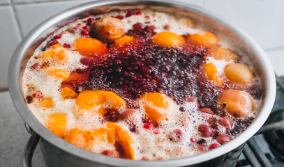Cooking a delicious compote of apricot, apples, cherries, raspberries. Fresh fruits are boiled in boiling water in a metal pan on the stove. Photography, concept.