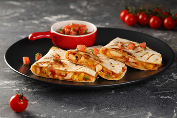 Grilled Quesadilla with chicken, cheese and vegetables. Served on a black plate with sauce of fresh tomatoes and herbs.