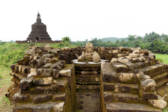 A ruined stone stupa with damaged Buddha statue in the centre, with West Myatazaung Pagoda in the background, Mrauk U, Rakhine, Myanmar (Burma), Asia