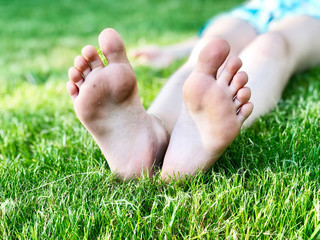 Barefoot kid lying on green grass against blurred background. Having fun outdoors in spring park