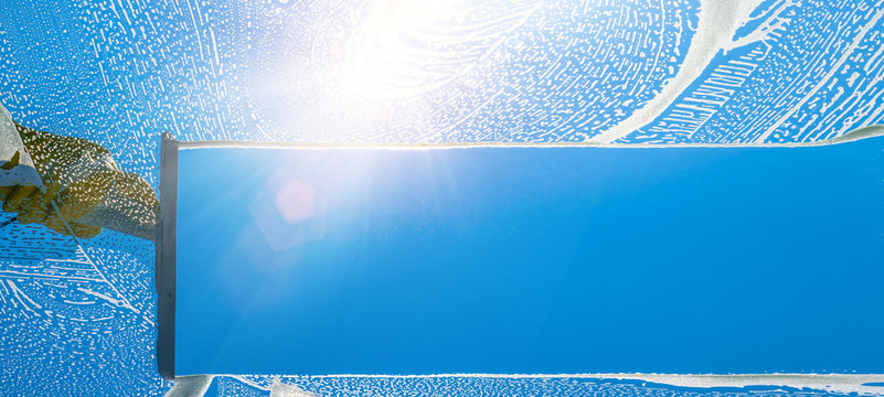 Window cleaner cleaning window with squeegee and wiper on a sunny day with a bright blue sky