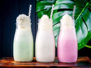 Set of different milkshakes with strawberries, mint and vanilla in glasses on a dark background with plants