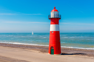 Fototapeta premium Sailship passing the Lighthouse in Westkapelle, Zeeland province, Netherlands. Westkapelle is a small city with about 2,600 inhabitants. The 16 meter tall cast iron lighthouse was built in 1875.