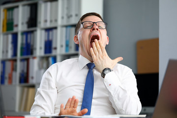Tired businessman office sits at table and yawns