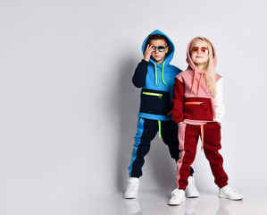 Little kids, boy and girl, in sunglasses and hoods, colorful tracksuits, sneakers. They posing...