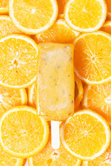 Yellow ice cream on a stick on a background of slices of orange. Hot summer concept. Top view, monochrome.