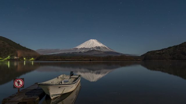 Mt Fuji under full moon with stars and fog at sunrise. Docked boat and reflection.