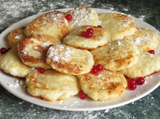 Cheesecakes on a plate, decorated with cranberries and icing sugar on top, on a background a green marble table and flour.