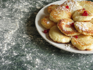 Cheesecakes on a plate, decorated with cranberries and icing sugar on top, on a background a green marble table and flour.
