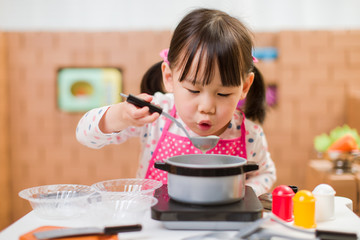 toddler girl pretend play food preparing role against cardboard blocks kitchen background