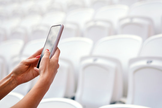 Girl uses a smartphone in a sports stadium on a background of empty plastic seats. Broadcasting a sporting event on social networks, live broadcast from the event.