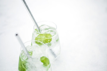 Beautiful glass of water or mojito with lime and mint cocktail on the gree background and white table summer vibe and atmosphere