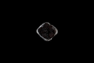 A portion of black raisins in a paper muffin cup on a black background.