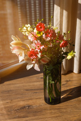 Flowers bouquet in the glass vase standing on the floor near the window. Big city life. Everyday romance. Beautiful sunlight.
