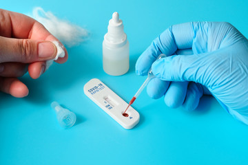 Express COVID-19 test for IgM and IgG antibodies to novel coronavirus SARS-CoV-2, Covid-19. Nurse hand in blue glove applies blood to test. Patient fingers with cotton. Vibrant turquoise background