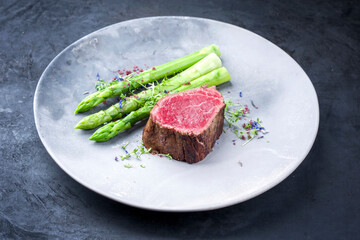 Gegrilltes dry aged Wagyu Filetkopf Medaillon Steak vom Rind natural mit grünen Spargel und Kräuter als closeup auf einem Modern Design Teller mit Textfreiraum