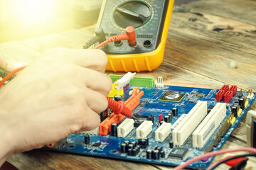 Engineer repairs a motherboard, he measures data with a multimeter.