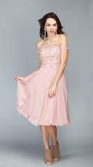Fototapeta premium Portrait of beautiful young european brunette girl in peach pink dress on grey background, prom dress