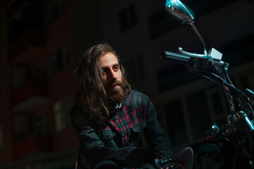 Night street portrait of young guy with long hair on a black motorcycle