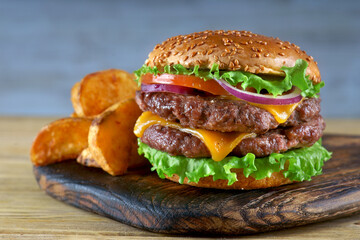 Double cheeseburger with fried potatoes on a light background