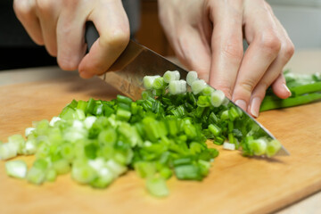 Women's hands cut green onions with a knife on a wooden Board close up